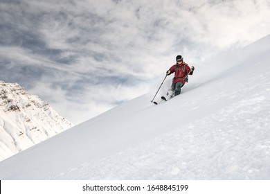 Smiling skiier in red jacket slides down the snowy mountain side