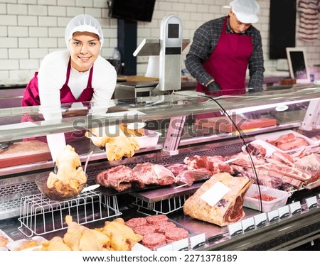 Smiling skilled young female butcher working behind counter in butchery, showing fresh gutted farm chickens