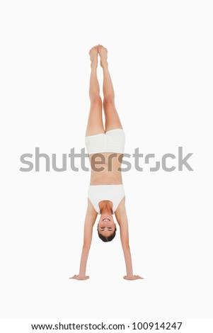 Smiling slim brunette handstands against white background