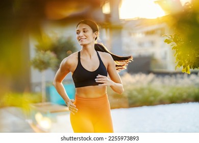 A smiling, slim female runner is running downtown on sunny day. - Shutterstock ID 2255973893