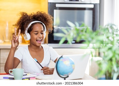Smiling small African American girl in headphones watch video lesson on computer in kitchen, happy little biracial child in earphones have online web class using laptop at home, homeschooling concept - Powered by Shutterstock