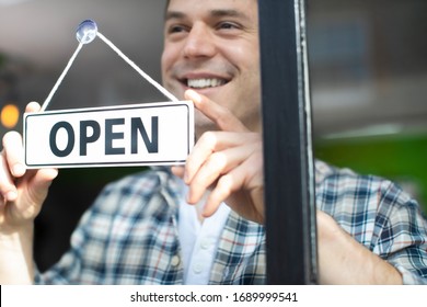 Smiling Small Business Owner Turning Around Open Sign On Shop Or Store Window Or Door