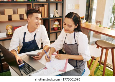 Smiling Small Business Owners Calculating Cafe Bills, Expenses And Taxes At Table