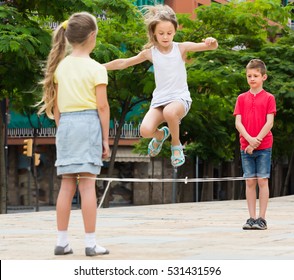 Smiling small kids in school age playing together with chinese jumping rope outdoors. Focus on boy