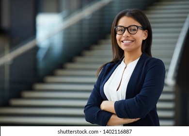 Smiling smart attractive young black lady in glasses standing in lobby and looking at camera, she working in prosperous company
