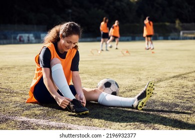Smiling soccer player tying her shoelaces on playing field. - Powered by Shutterstock