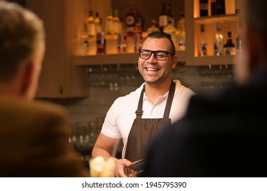a smiling and sociable bartender conducts a conversation with customers in the bar. Evening in the restaurant, communication of bar guests with the bartender - Shutterstock ID 1945795390