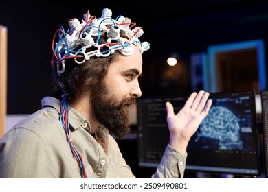 Smiling software technician using EEG headset to upload consciousness into computer. Happy IT admin working with AI, using high tech gear to create connection between brain and PC