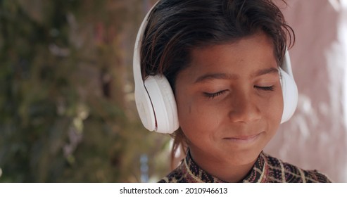 A Smiling South Asian Child Listening To Music With Headphones