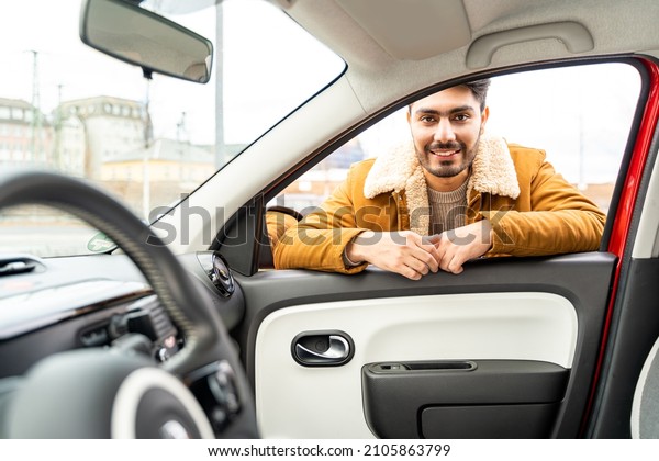 Smiling spanish or arab eastern ethnicity cheerful\
man in yellow jacket leaned on door looking through window of car\
as passanger asking for ride or driver. Travel, exam, lesson,\
learning, taxi driver