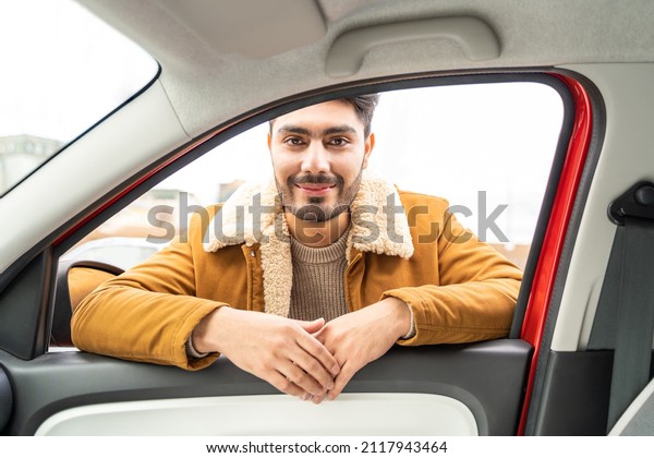 Smiling spanish or arab eastern ethnicity man in\
casual clothes leaned on door looking through window of car as\
passanger asking for ride or driver. Travel, exam, lesson,\
learning, taxi driver