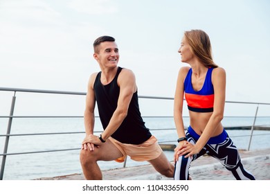 Smiling sportive couple doing sports exercises, looking at each other, while stretching a body, during workout on the quay. - Shutterstock ID 1104336590
