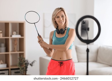 Smiling sports blogger holding badminton racket while streaming online fitness lesson with smartphone at home - Powered by Shutterstock