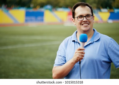 Smiling Sportscaster With Microphone Is Reporting From Stadium.