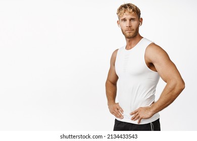 Smiling Sportsman Holding Hands On Waist, Listening Music In Wireless Earphones, Workout In Gym, Standing In Tank Top And Shorts Against White Background