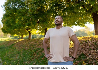 Smiling sportsman resting in the park on a run, man breathing fresh air enjoying an active lifestyle, hispanic man exercising.