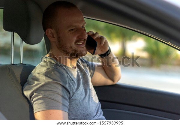 Smiling sportsman sitting in car and using\
mobile.Side view of successful man sitting in luxury car and\
talking on phone,copy space.Distracted man in car checking phone\
while driving during the\
day.