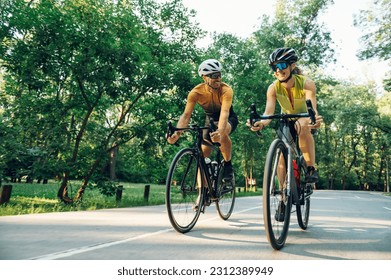 Smiling sporty couple on bicycles during weekend cycle ride while wearing sports clothes and helmets. Traveling by high-performance sport bicycles. Sports and healthy lifestyle. Copy space. - Shutterstock ID 2312389949