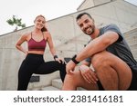 Smiling sporty couple resting after a workout, enjoying a healthy lifestyle after training together. Young male and female runners dressed in sportswear looking at camera. Athletic personal trainer