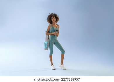 Smiling sporty woman with sports bag and bottle of water after training on studio background - Shutterstock ID 2277328957