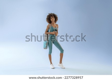 Smiling sporty woman with sports bag and bottle of water after training on studio background