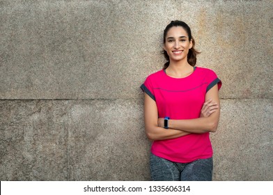 Smiling Sporty Young Woman Take A Break After Running. Confident Latin Girl Leaning Against Wall In Sportswear. Portrait Of Happy Runner Looking At Camera And Smiling With Crossed Arms, Copy Space.