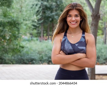 Smiling sporty young woman working out outdoors and looking at camera. Confident Hispanic girl sportswear training. Portrait of happy runner with crossed arms in an urban park. Copy space