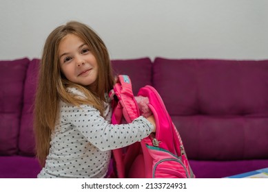 Smiling Student Girl Learning In The Home. Happy Child Girl Packing School Bag. Happy Kid Arrange Book In Backpack While Readying For School.