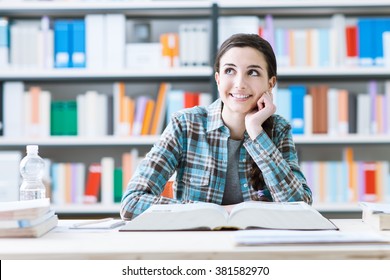 Smiling Student Girl In The Library Studying And Day Dreaming, She Is Thinking With Hand On Chin And Looking Up, Education And Future Concept