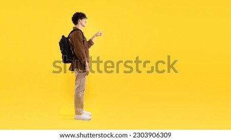 Smiling Student Guy With Backpack Pointing Finger Aside At Empty Space For Text, Showing Great Educational Offer Or Course Advertisement Standing On Yellow Studio Background. Side View, Panorama