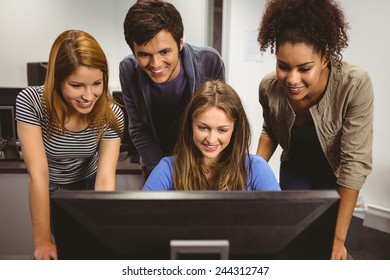 Smiling students sitting at desk using computer together in classroom