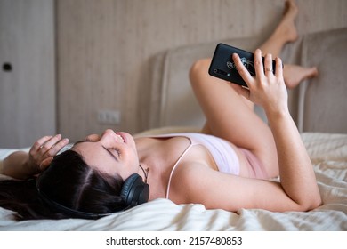 Smiling Stunning Woman Laying Down In Bed Listening Music On The Phone In Headset