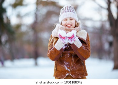 smiling stylish girl with mittens in a knitted hat and sheepskin coat playing outside in the city park in winter.