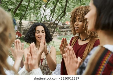 smiling and stylish interracial women praying together outdoors in retreat center
