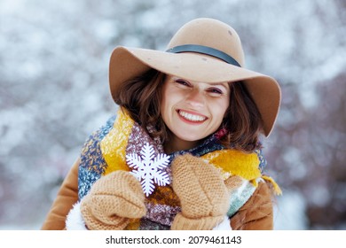 Smiling Stylish Middle Aged Woman In Brown Hat And Scarf With Mittens And Snowflake In Sheepskin Coat Outdoors In The City Park In Winter.