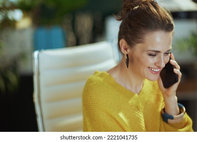 Smiling Stylish Small Business Owner Woman In Yellow Sweater In The Modern Green Office Speaking On A Smartphone.