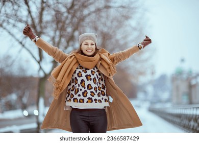 smiling stylish woman in brown hat and scarf in camel coat with gloves and raised arms rejoicing outside in the city in winter. - Powered by Shutterstock