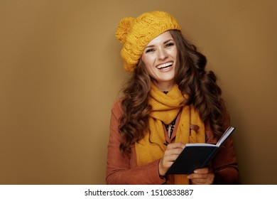 Smiling Stylish Woman In Yellow Beret And Scarf Writing Personal Goals In Notebook On Beige Background.