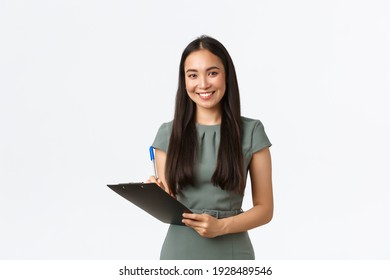 Smiling successful asian businesswoman writing down clients info, holding clipboard and pen, fill in papers for client shipping of parcel, looking upbeat working from home, own online store