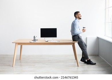 Smiling Successful Bearded Man In Formalwear Sitting Leaning On Table, Drinking Coffee Looking At Window, Showing Pc With Blank Black Mock Up Screen At Home Office, Free Copy Space, Full Body Length - Powered by Shutterstock