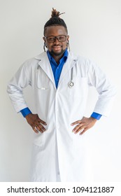 Smiling Successful Black Male Doctor In Lab Coat Holding Hands On Hips And Looking At Camera. Content Confident Young African Medical Specialist Standing Like Superhero. Leading Doctor Concept