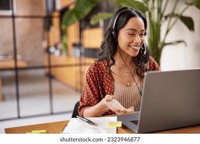 Smiling successful business woman with headphones talking while attending a meeting online using laptop. Hispanic businesswoman watch webinar and listen online course. Latin woman using computer. - Powered by Shutterstock