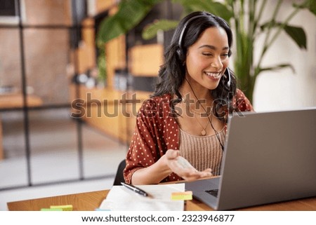 Smiling successful business woman with headphones talking while attending a meeting online using laptop. Hispanic businesswoman watch webinar and listen online course. Latin woman using computer.