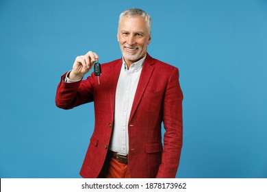 Smiling successful cheerful elderly gray-haired mustache bearded business man wearing red jacket suit standing hold in hand car keys looking camera isolated on blue color background studio portrait