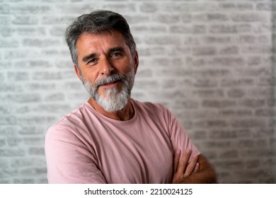 Smiling successful confident mature bearded casual business man wearing pink t-shirt holding hands crossed isolated on grey color background studio portrait. Achievement career wealth concept