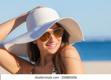 smiling summer woman on beach with sunglasses and floppy hat