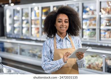 Smiling supermarket employee using a tablet in front of the frozen food section. Friendly staff providing excellent customer service and managing inventory in a grocery store. - Powered by Shutterstock