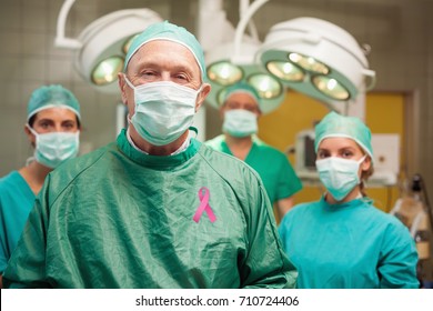 Smiling surgeon posing with a team against breast cancer awareness message