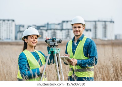 Smiling surveyors with digital level and tablet looking at camera in field