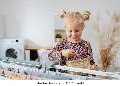 Smiling Sweet Blue-eyed Girl Spends Time In The Bathroom, Laundry Room Picking Out A Clip To Put On Already Washed Clothes Hanging On The Dryer, Helping With Household Chores